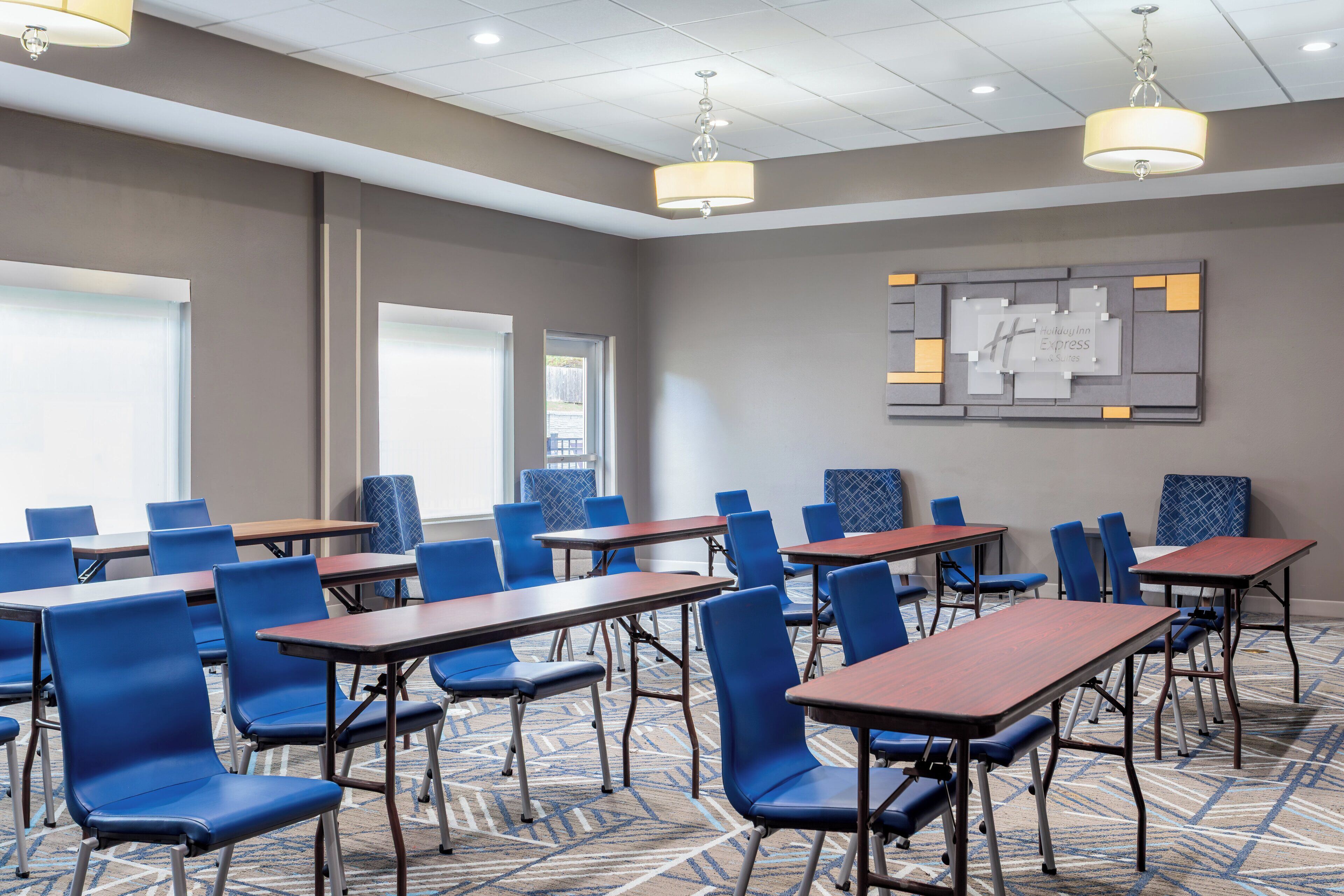 A conference room with blue chairs and wooden tables, a patterned carpet, and a wall-mounted sign.