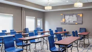 A conference room with blue chairs and wooden tables, a patterned carpet, and a wall-mounted sign.