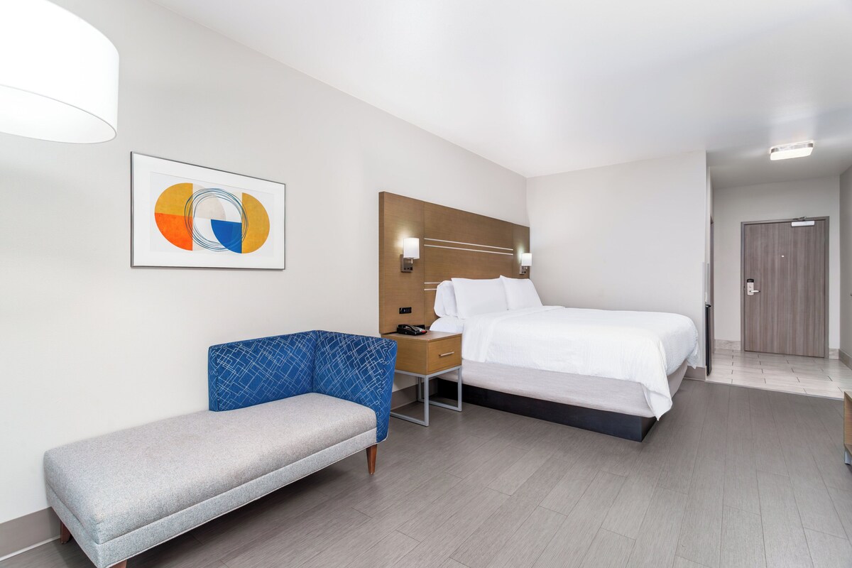 Habitación de hotel moderna con cama, banqueta, escritorio y una obra de arte colgada en la pared.