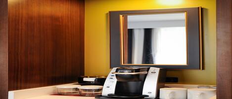 A coffee maker on a countertop with a mirror above it.