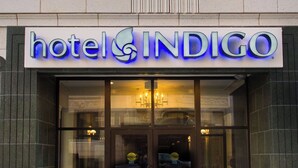 A hotel entrance with a sign reading 'hotel INDIGO,' large glass doors, and a reflection of a car in the window. - Hotel Indigo Kansas City Downtown by IHG (Kansas City)