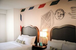 Ein Hotelzimmer mit zwei Betten, einem Nachttisch mit Lampe sowie einer Wand mit einem Willkommensschild und einem Stempel.