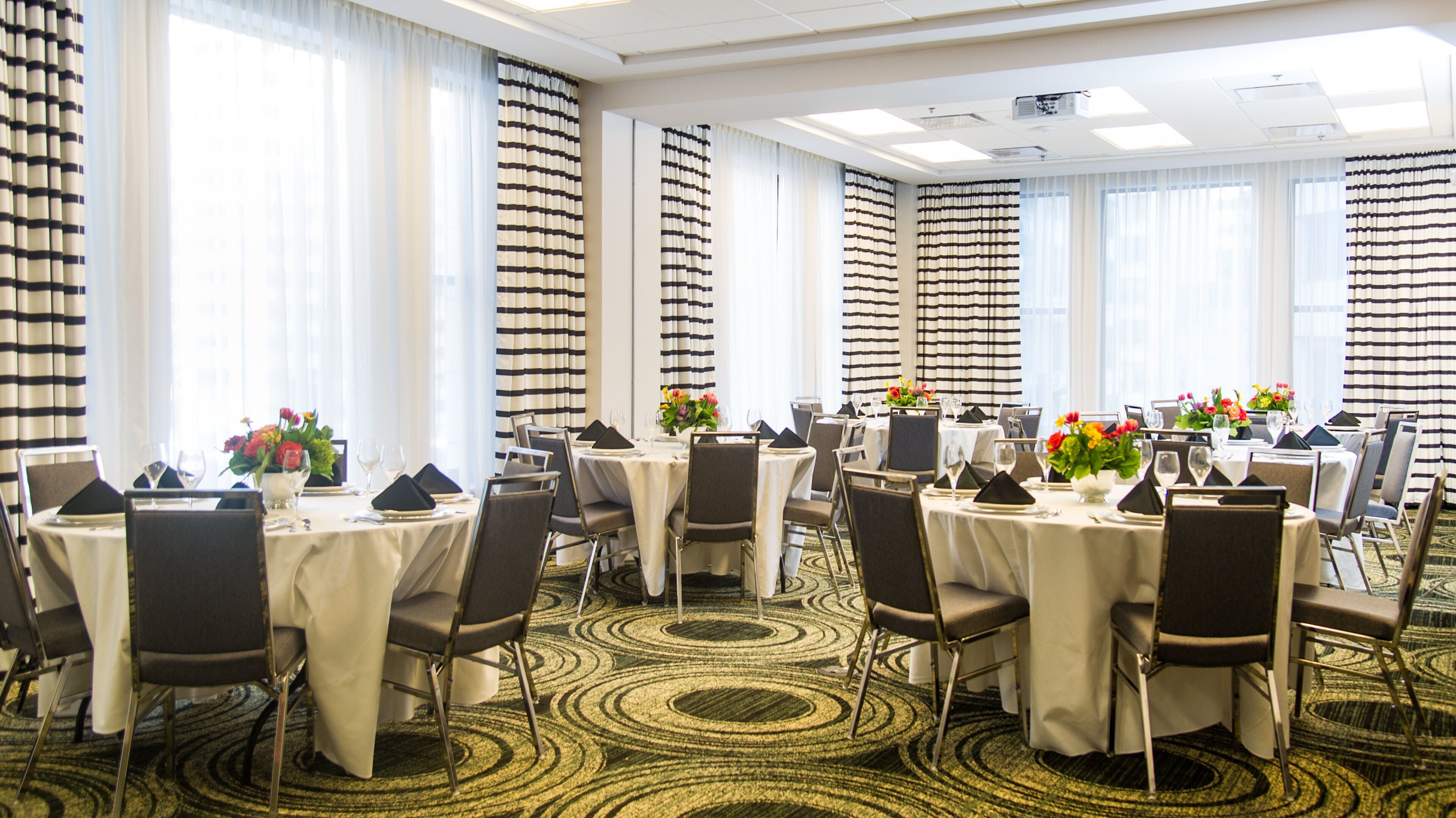 Un salón de conferencias de hotel con mesas redondas, sillas y piso alfombrado.