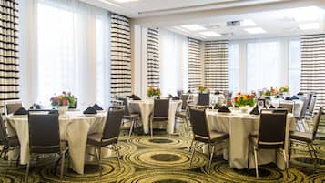 Un salón de conferencias de hotel con mesas redondas, sillas y piso alfombrado.