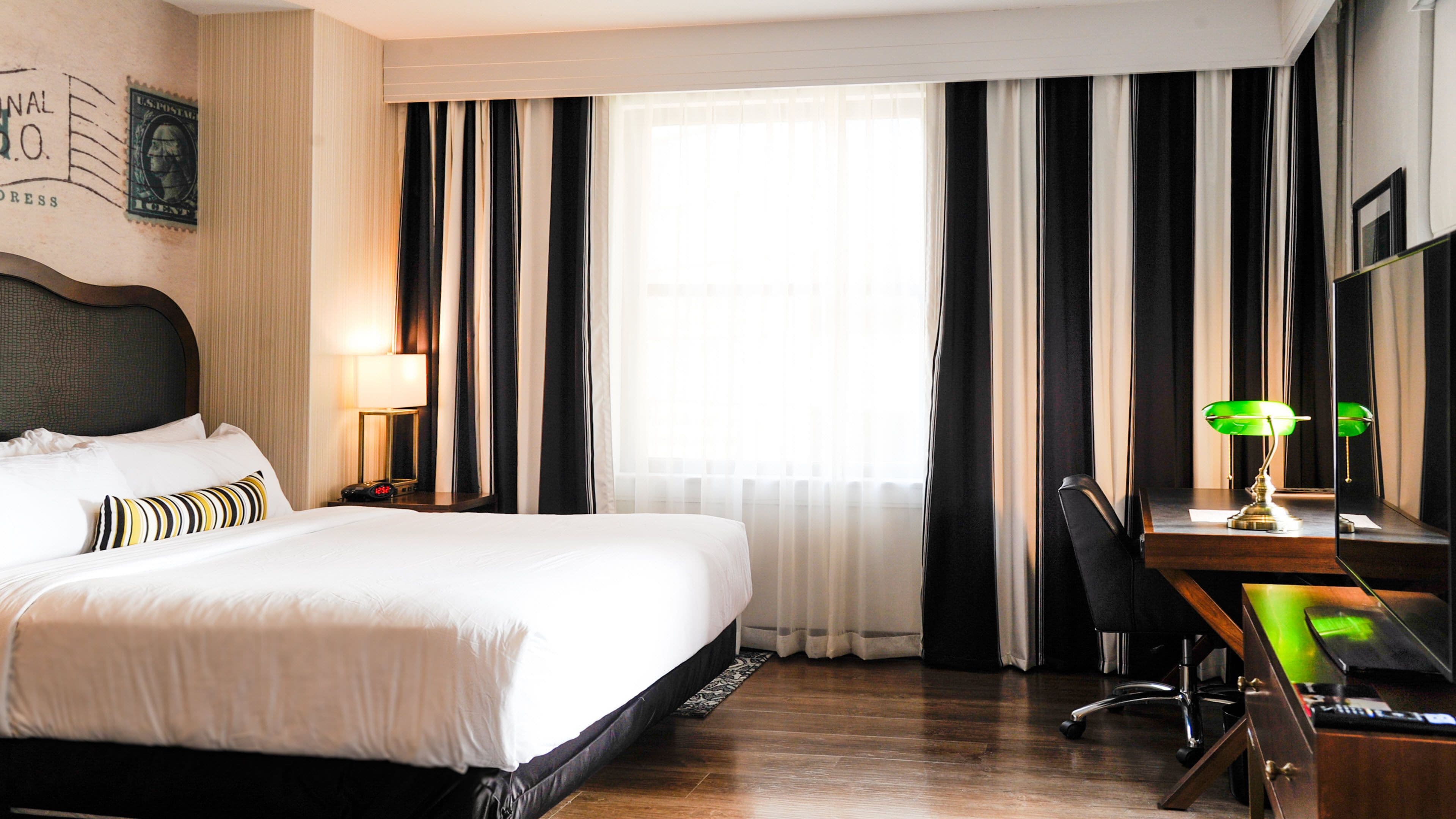 Une chambre d’hôtel avec un grand lit, un bureau avec une chaise, une lampe et un miroir.