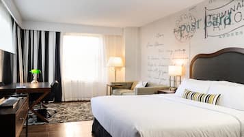 A hotel room with a large bed, a desk, a chair, a lamp, and a wall with handwritten notes.