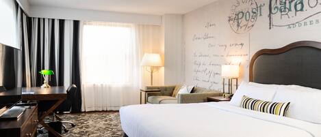 A hotel room with a large bed, a desk, a chair, a lamp, and a wall with handwritten notes.