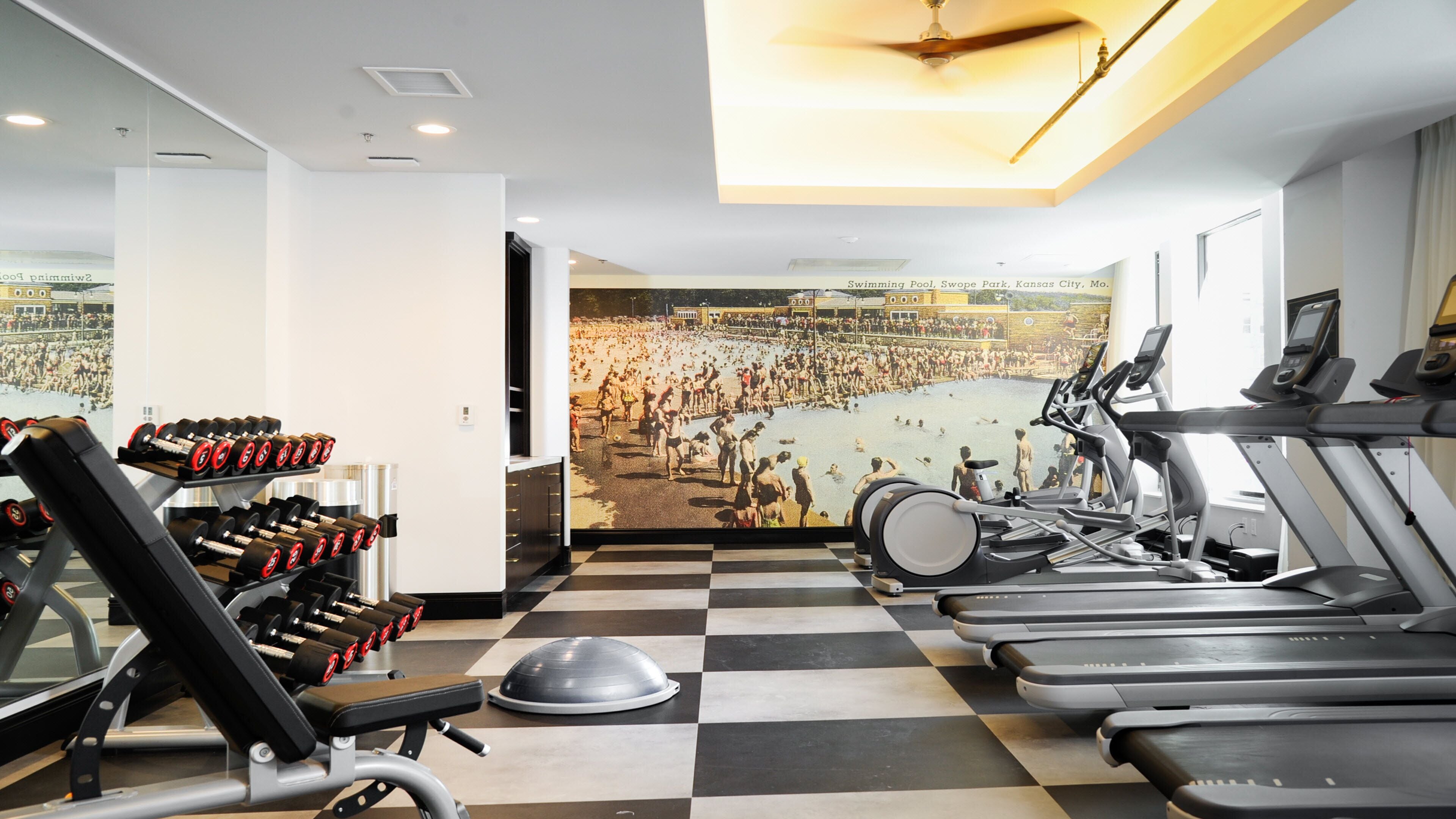 A gym with treadmills, dumbbells, and a mural of a swimming pool.
