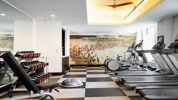 A gym with treadmills, dumbbells, and a mural of a swimming pool.