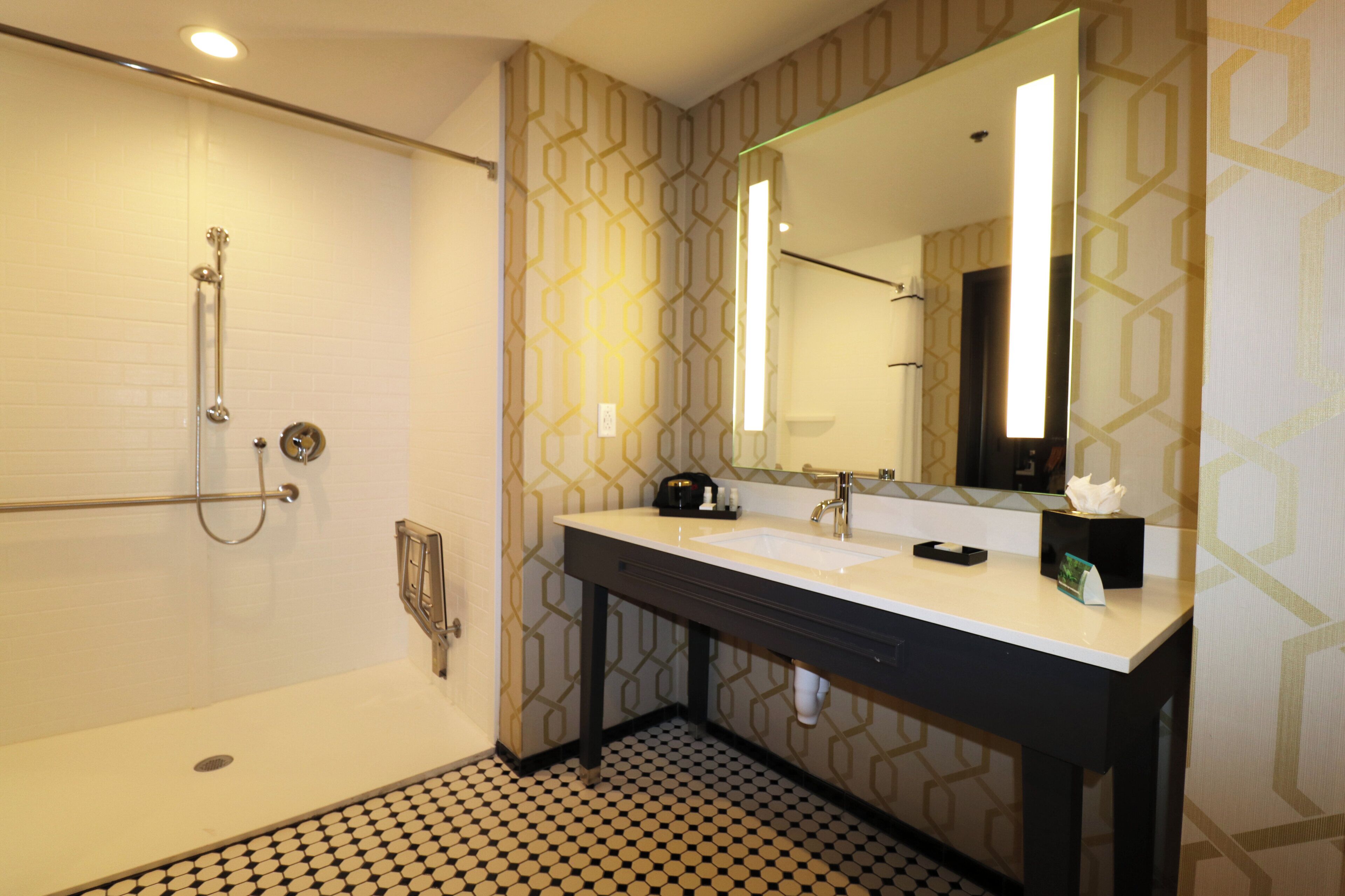 Een badkamer met een douche, wastafel, spiegel en een vloer met een patroon.