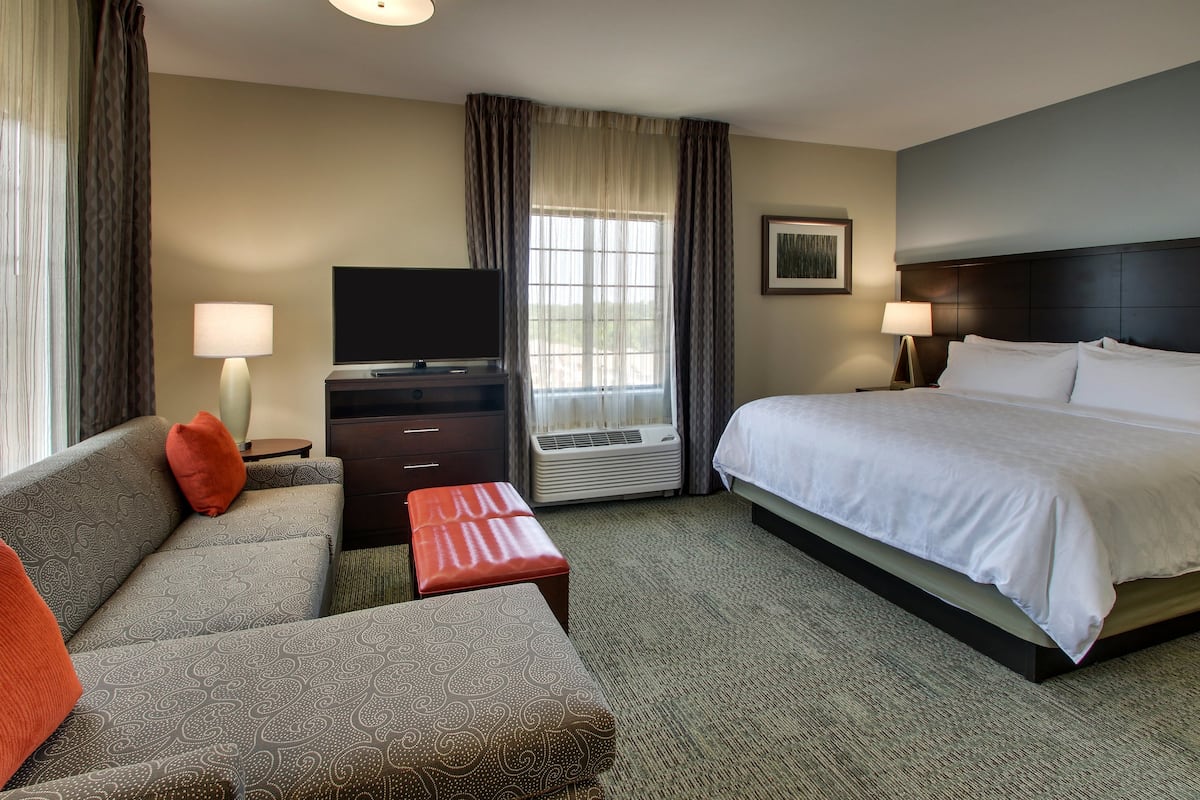 Une chambre d’hôtel avec un lit, un canapé, une télévision, un bureau et une fenêtre avec des rideaux.