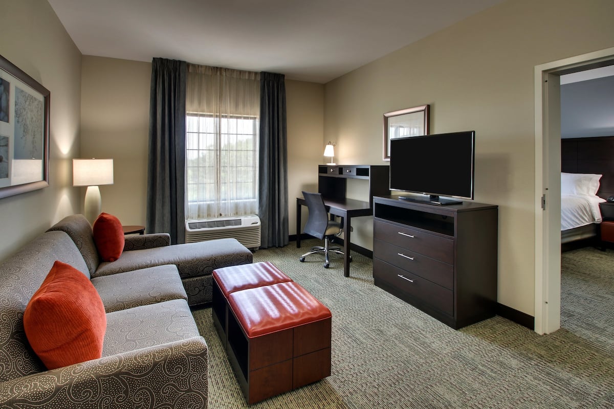 Une chambre d’hôtel équipée d’un canapé, d’un pouf, d’un bureau, d’une télévision et d’un lit.