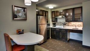 Une cuisine moderne dotée d’un réfrigérateur en acier inoxydable, de meubles de cuisine en bois foncé, d’un plan de travail blanc et d’un coin repas avec une chaise et une table.