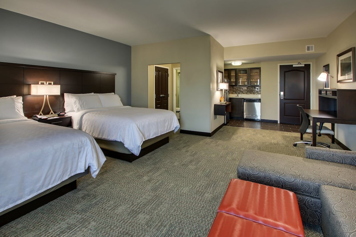 Une chambre d’hôtel avec deux lits, un bureau, une chaise et une kitchenette.