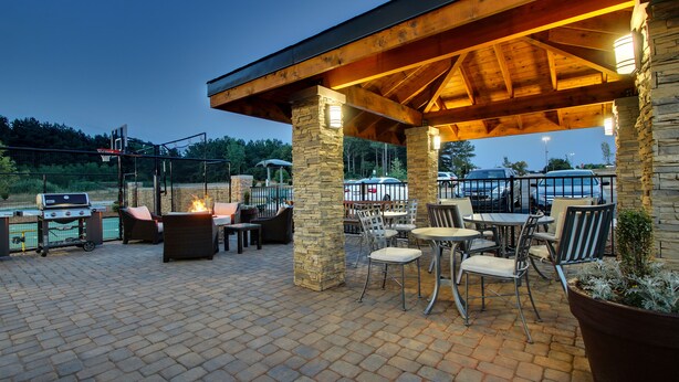 Une terrasse extérieure avec des piliers en pierre, des tables et des chaises en métal, un barbecue et un foyer.