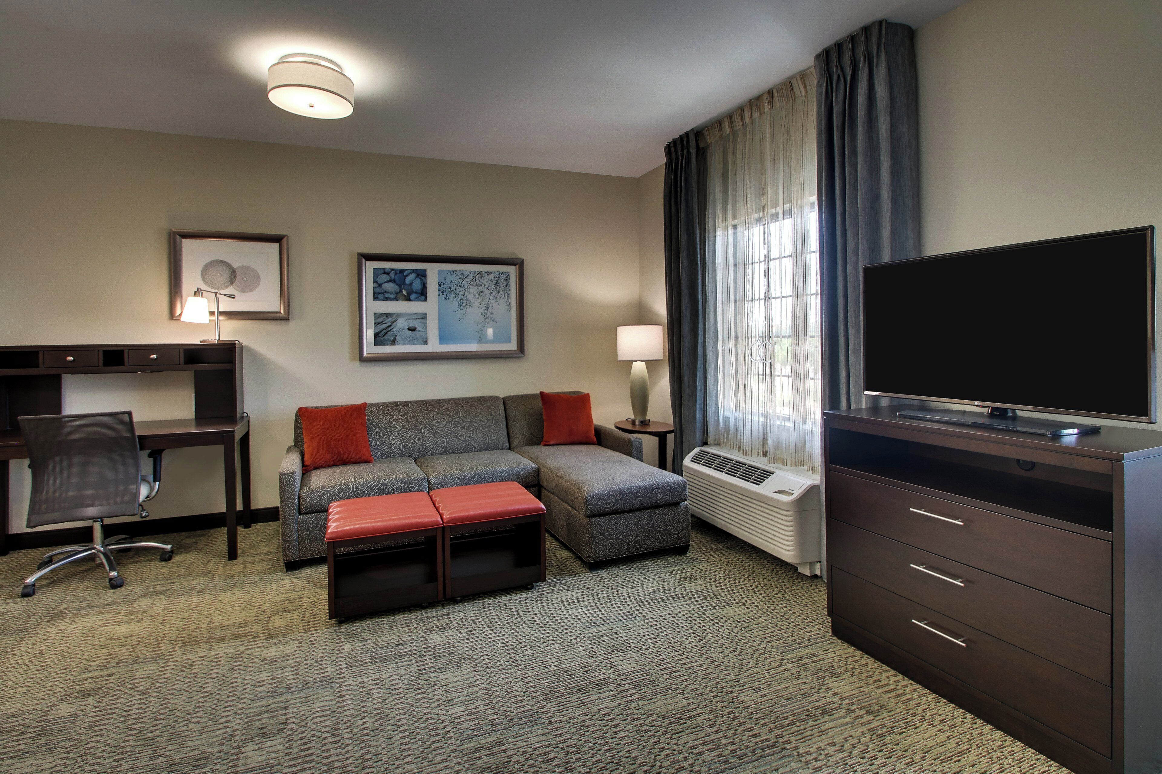A hotel room with a sofa, a desk, a television, and a window with curtains.