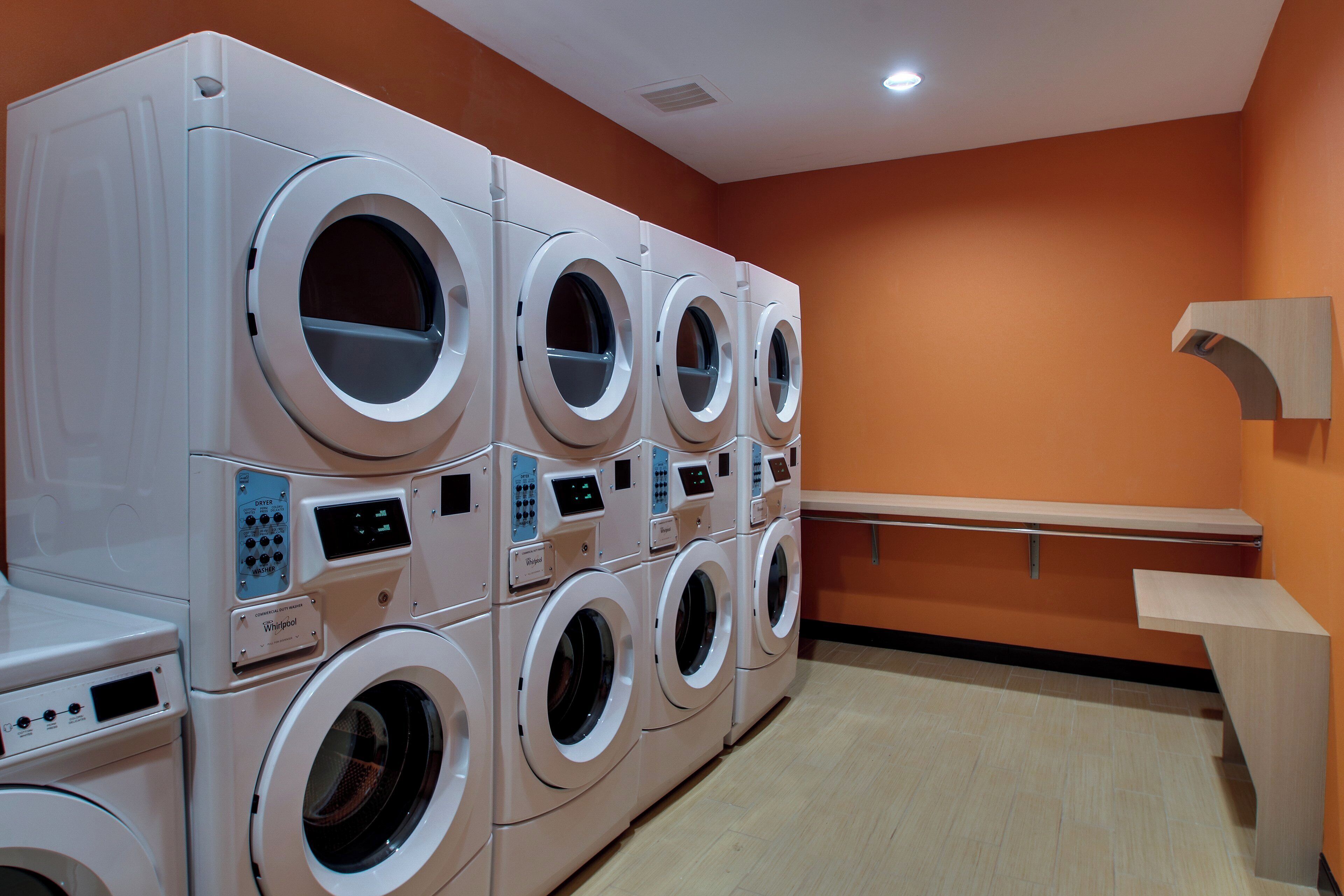 A laundry facility with multiple washing machines and dryers, a bench, and a wall-mounted towel rack.
