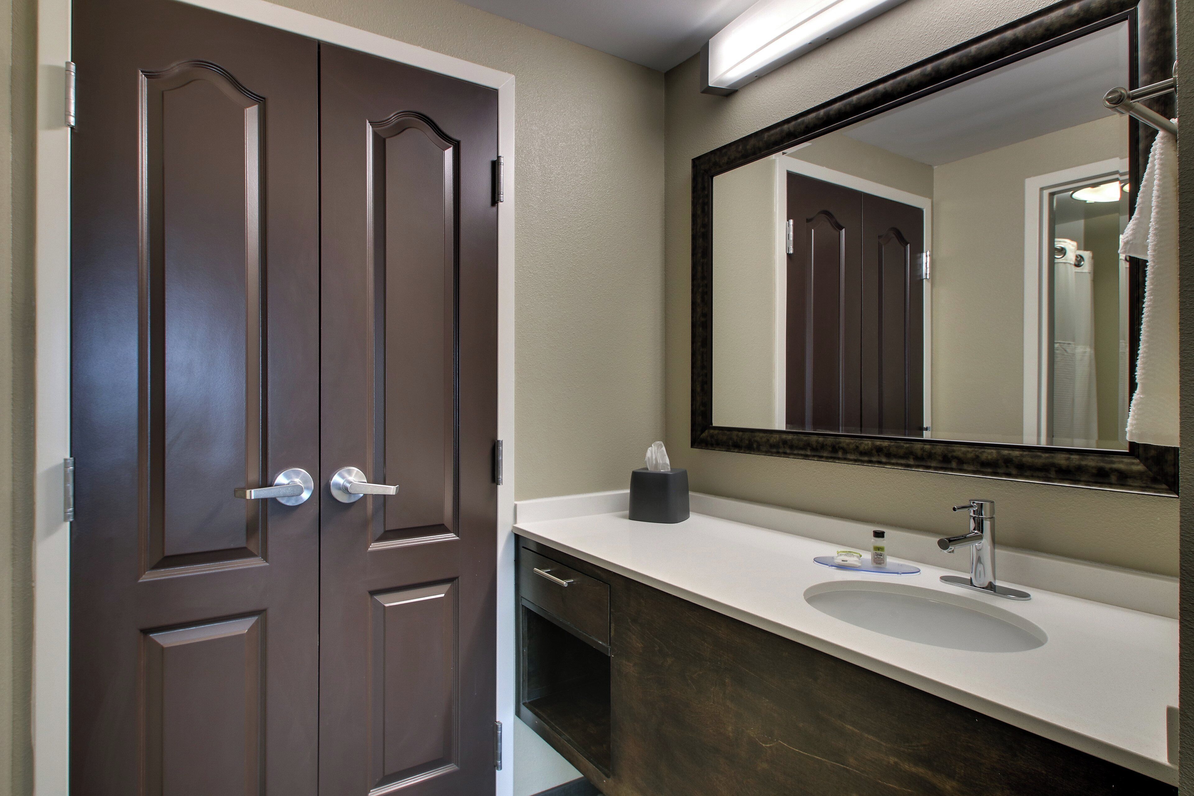 A bathroom with a double door, a sink, a mirror, and a towel hanging on the wall.