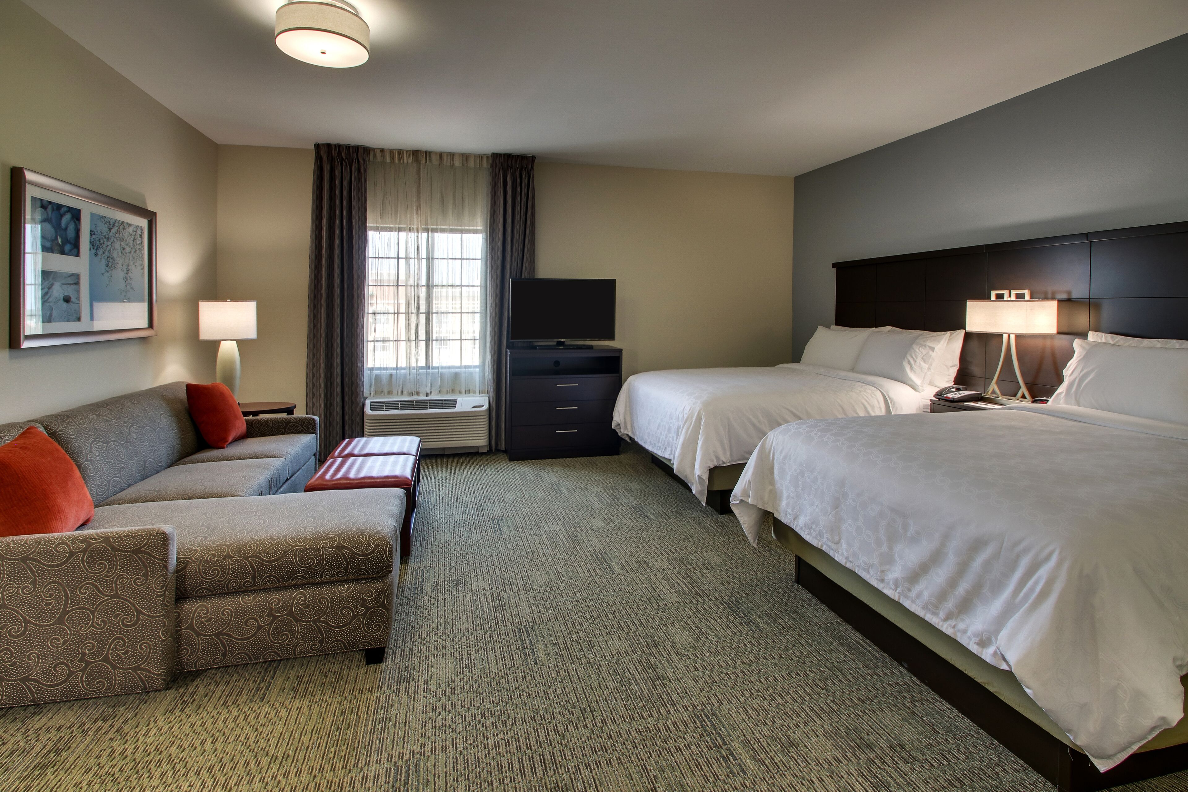 A hotel room with a sofa, two beds, a TV, a desk, and a lamp.