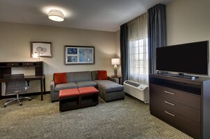 Quarto de hotel com sofá, escrivaninha, televisão e luminária.