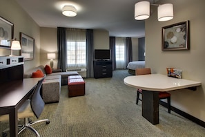 Una habitación de hotel con escritorio, sofá, mesa de comedor, televisor y cama.