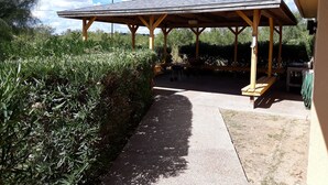 A covered outdoor seating area with a wooden roof and benches, surrounded by dense shrubbery and a clear sky. - Sunbridge Inn & Suites (Zapata)