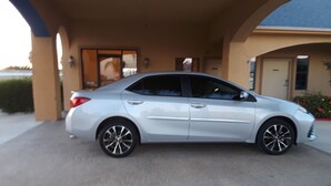 A white sedan parked under a covered area with a building in the background. - Sunbridge Inn & Suites (Zapata)