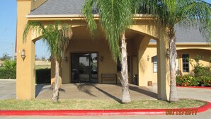 A building with a yellow facade, a covered entrance, and palm trees in front. - Sunbridge Inn & Suites (Zapata)