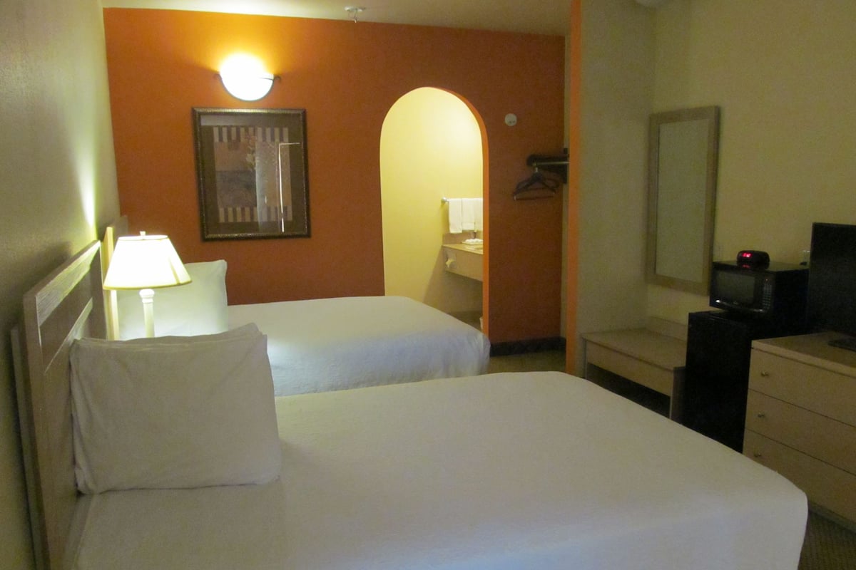 A hotel room with two beds, a desk with a television, a mirror, and a lamp.