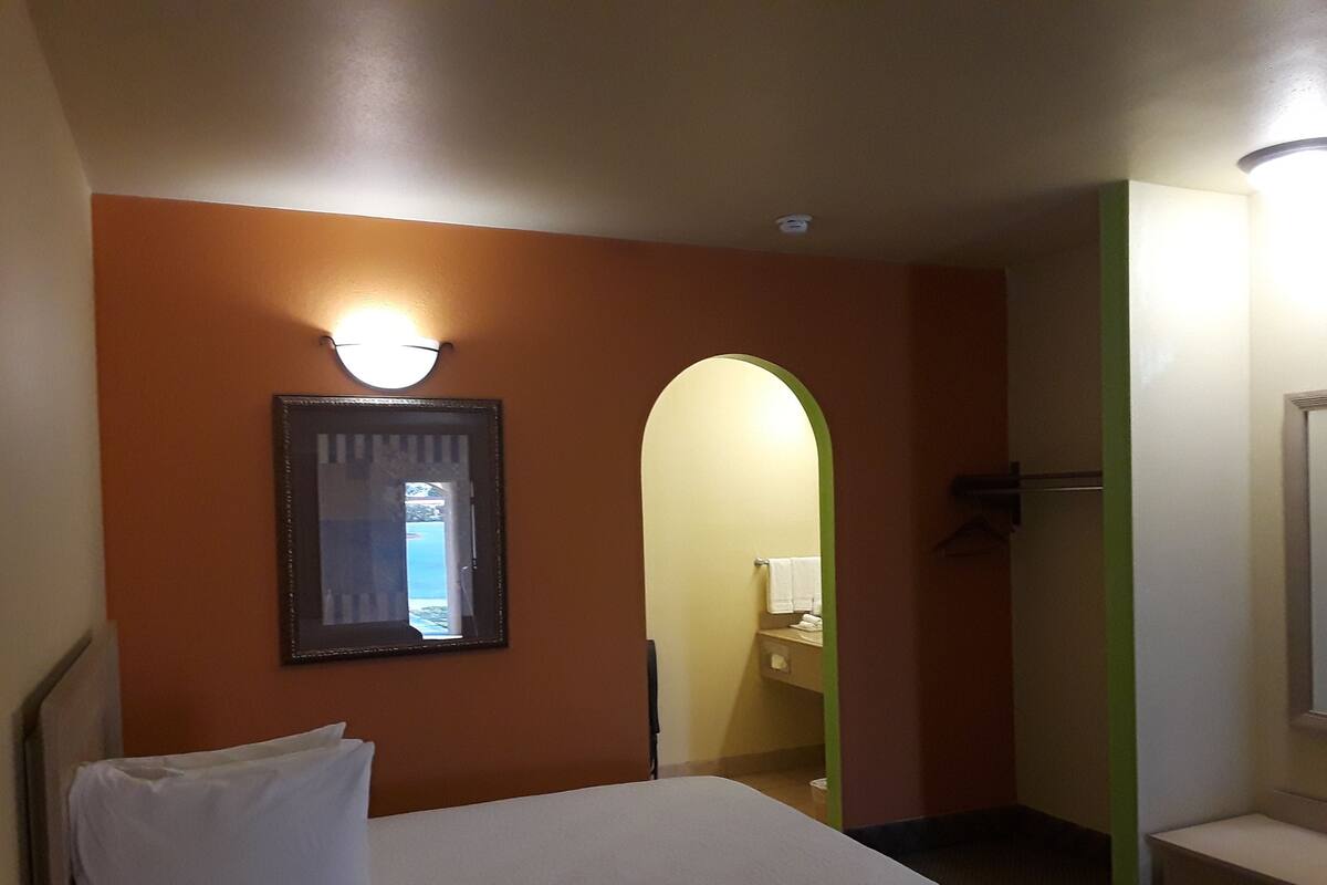 A hotel room with a bed, a wall-mounted light, a mirror, and a door leading to a bathroom.