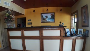 A reception desk with a wooden panel design, a framed painting of a beach scene, and a vase with flowers on the left. - Sunbridge Inn & Suites (Zapata)