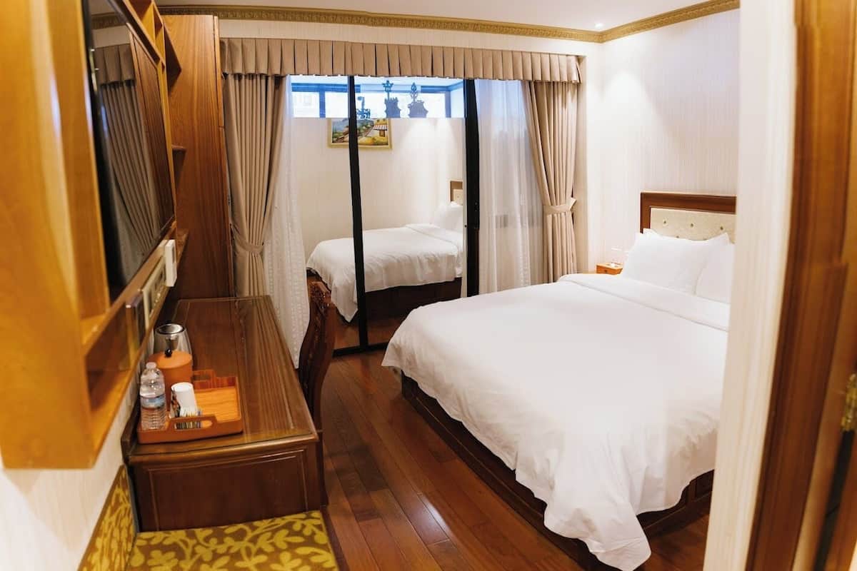 Una habitación de hotel con dos camas, un escritorio de madera, una mesita y una ventana con cortinas.