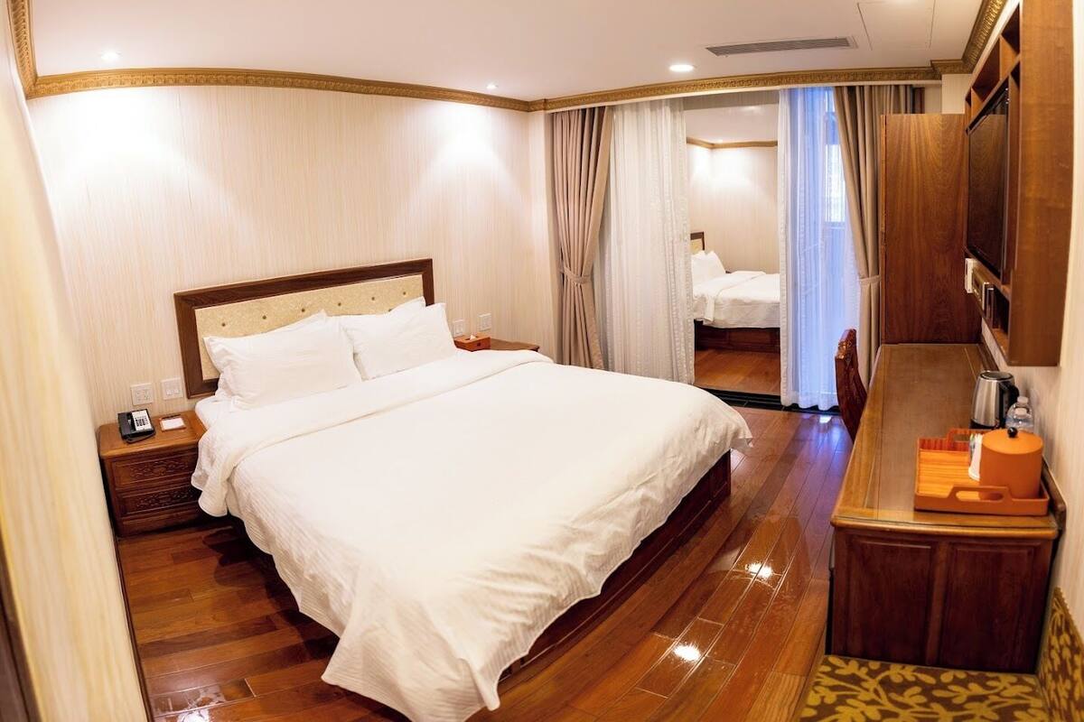 Una habitación de hotel con una cama grande, una mesita de noche de madera, un escritorio con un hervidor y un espejo.