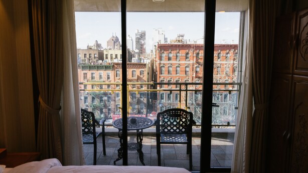 Habitación de hotel con balcón, cama y vistas a edificios de la ciudad.