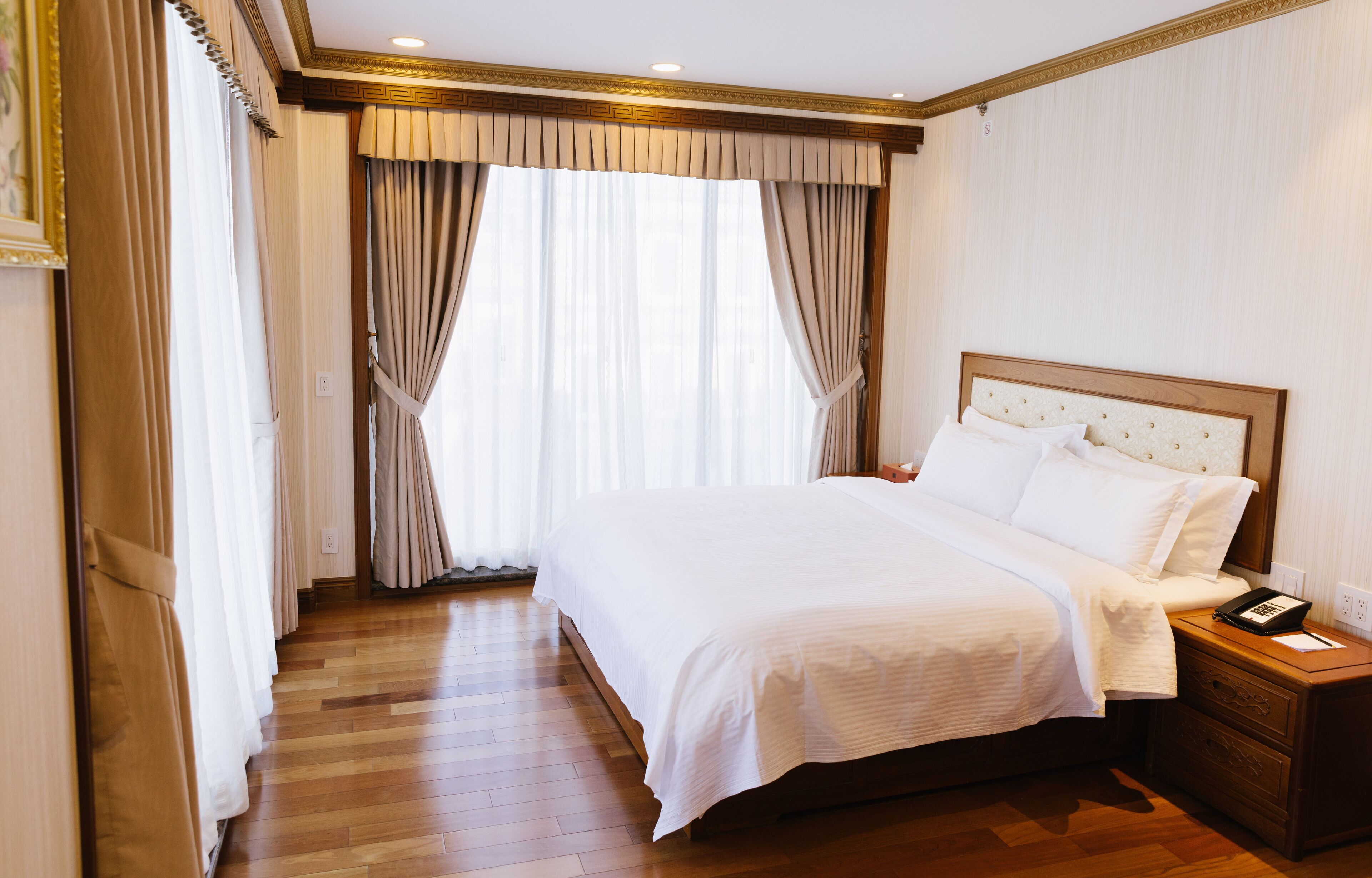 Habitación de hotel con una cama grande, suelo de madera, cortinas y un teléfono en la mesita de noche.