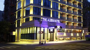 Un hotel de varios pisos con diseño moderno, con balcones en cada planta y una entrada destacada con un letrero.