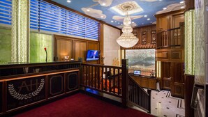 Un vestíbulo de hotel con alfombra roja, paneles de madera, un candelabro y una pantalla de televisión.