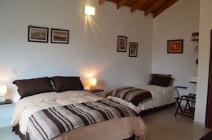 A bedroom with two beds, a nightstand with a lamp, and framed pictures on the wall. - El Chalten Aparts (El Chalten)