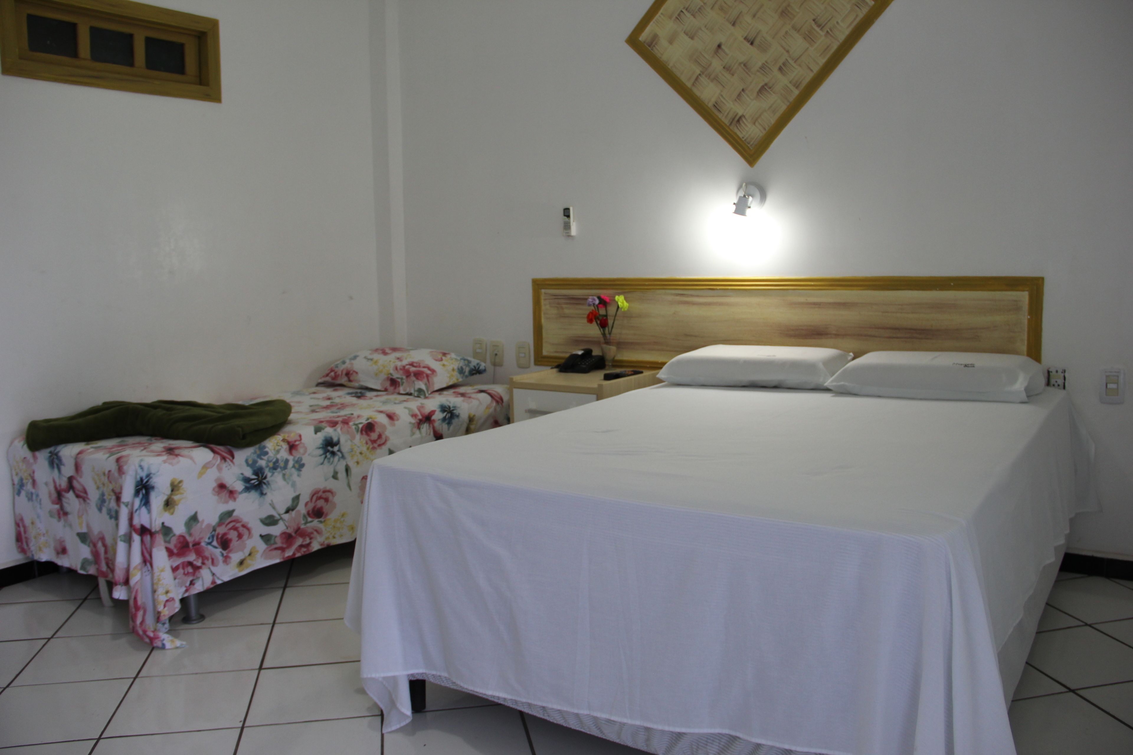 A hotel room with a large bed, a smaller bed, and a nightstand with a lamp.