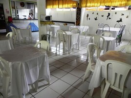 Un comedor con varias mesas y sillas, una cocina al fondo y una pared decorada con pájaros.