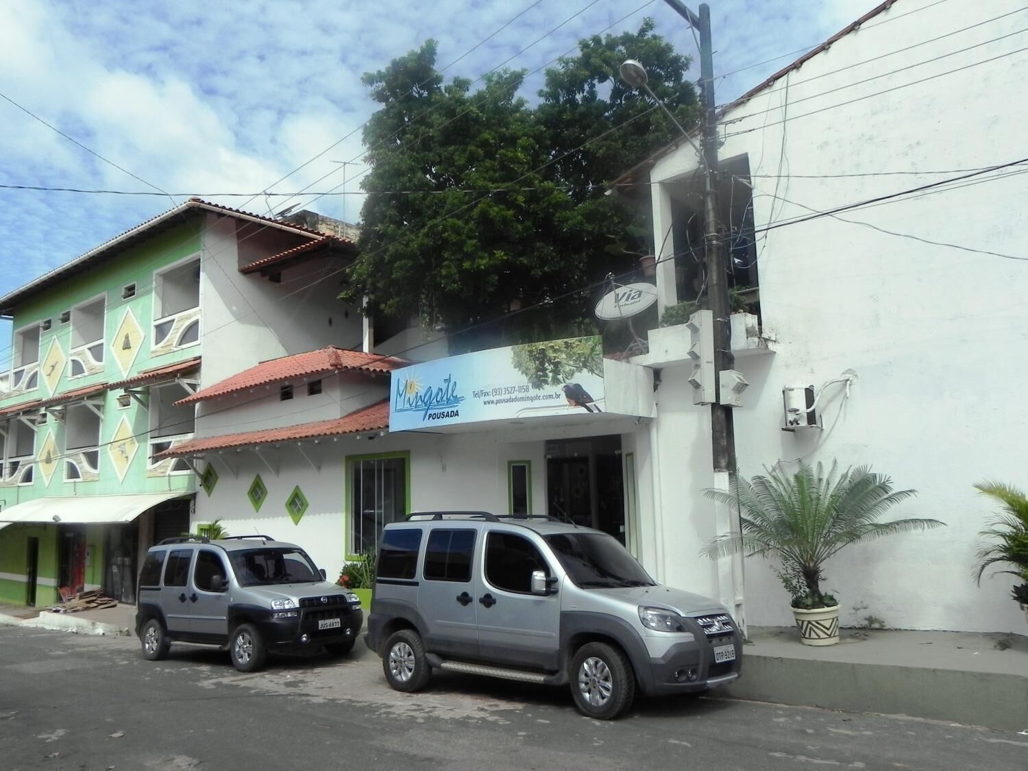 A building with a sign for 'Mingate Pousada' and two parked SUVs.