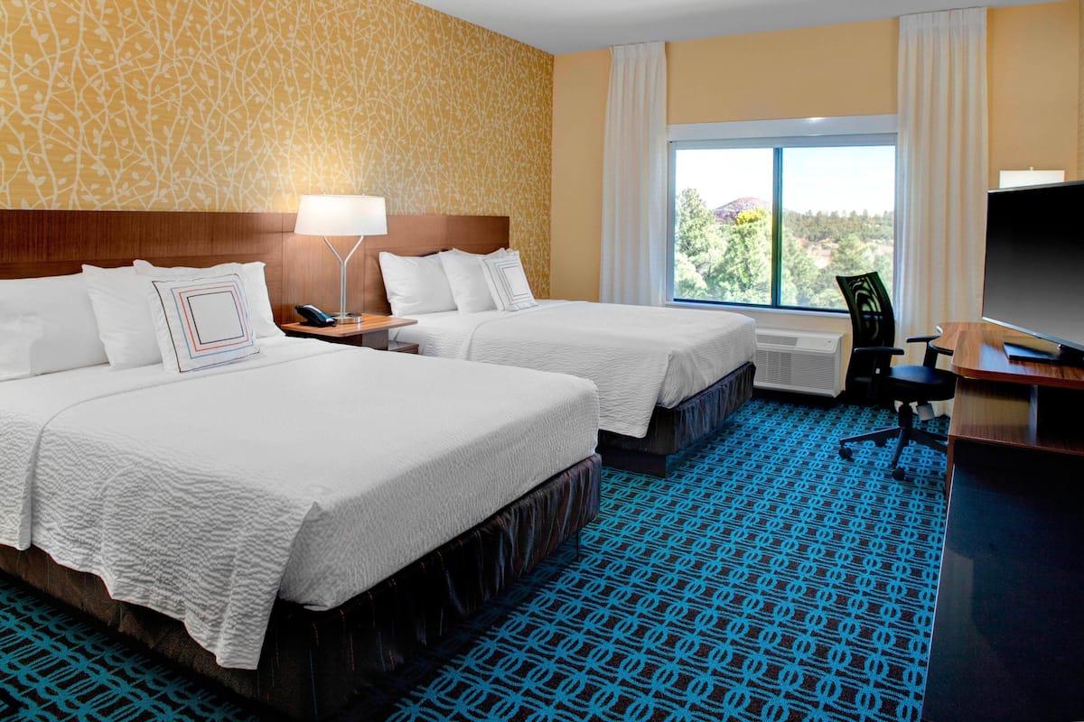 A hotel room with two beds, a desk, a chair, a TV, and a window with a view.
