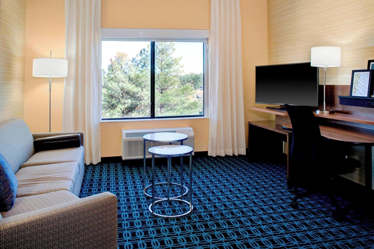 A hotel room with a sofa, a small table, a TV, and a desk with a chair.