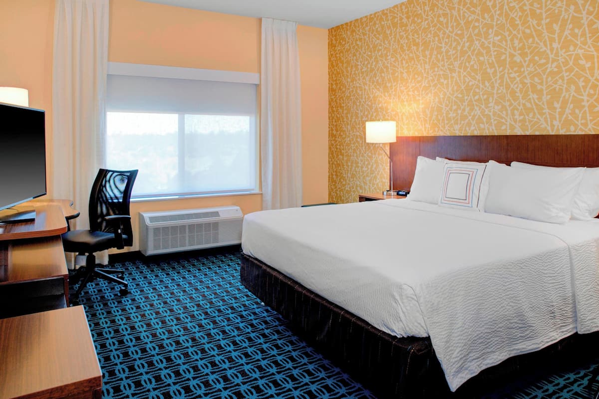 A hotel room with a large bed, a desk with a chair, a TV, and a window with curtains.