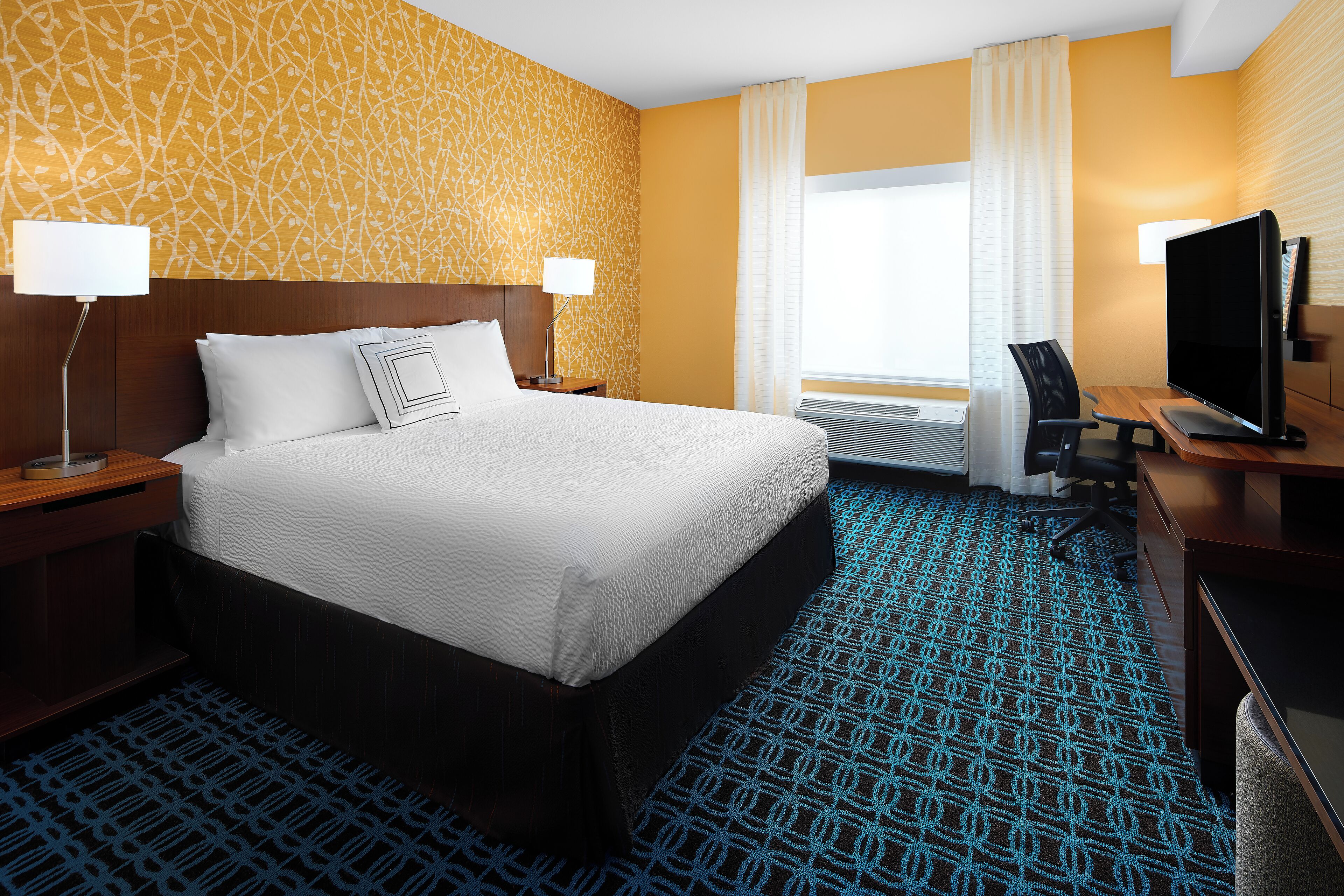 A hotel room with a large bed, two bedside tables with lamps, a desk with a computer, and a TV.