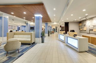 A modern hotel lobby with a reception desk, seating area, and a dining area.