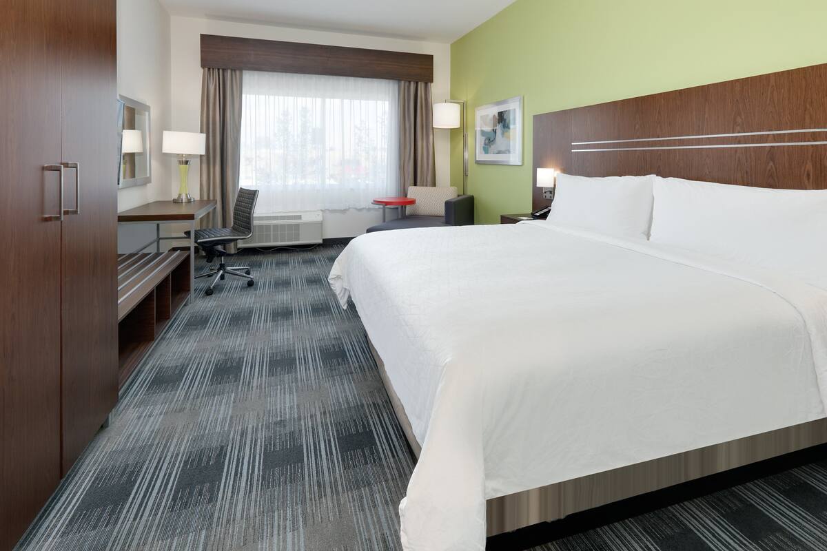 A hotel room with a large bed, a desk with a chair, a small table, and a couch.