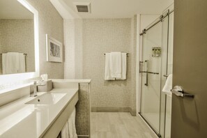 A modern bathroom with a large mirror, a sink, a shower, and a towel rack. - Holiday Inn Express & Suites Dallas NW - Farmers Branch by IHG (Farmers Branch)