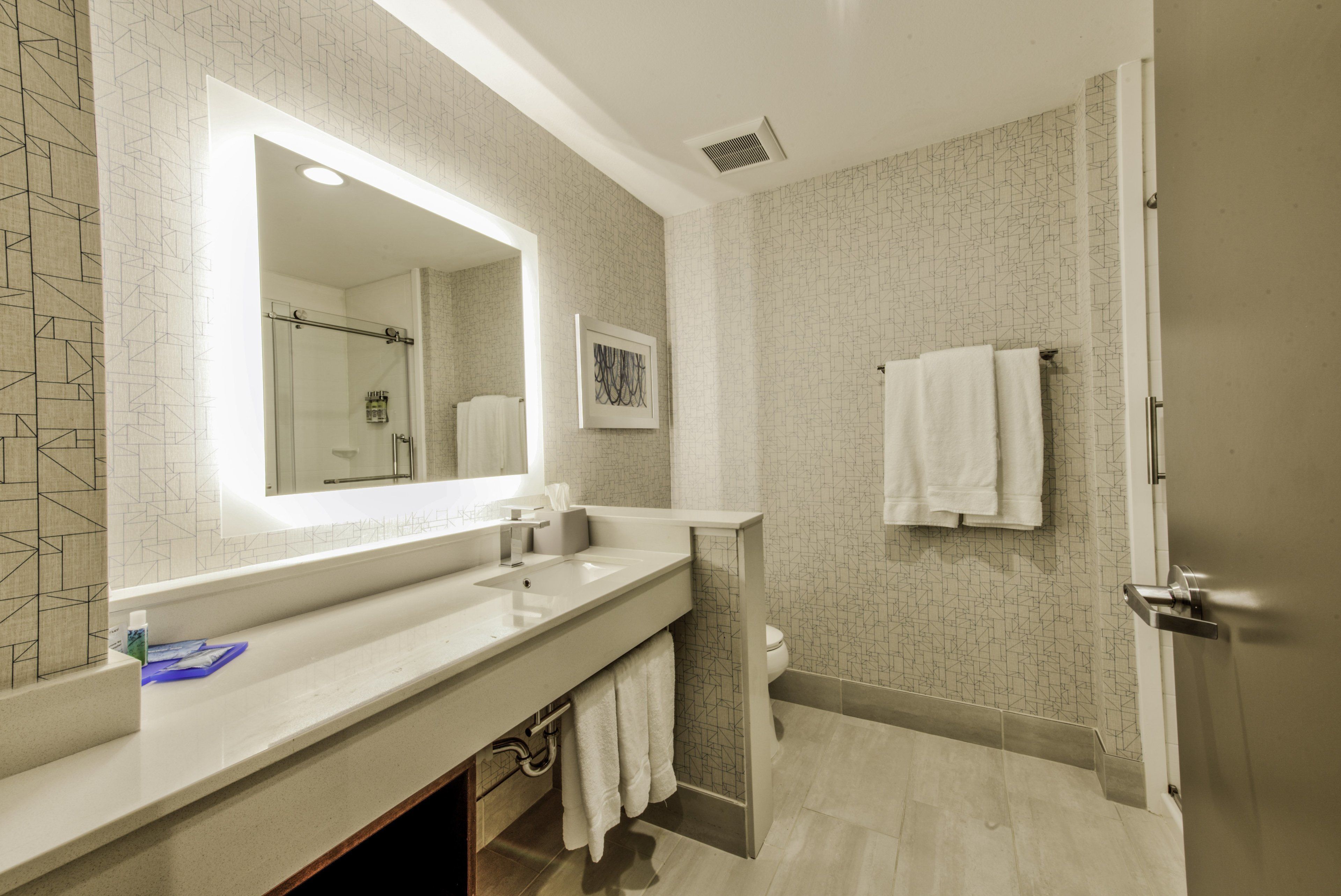 A modern bathroom with a large mirror, a double sink, a shower, and a toilet.