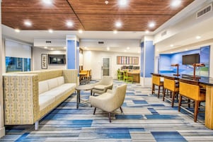A hotel lobby with a sofa, chairs, a coffee table, a reception desk, and a TV screen.